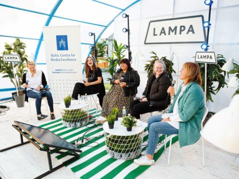 Āra paneļdiskusija, kurā piecas sievietes sēž un iesaistās sarunā. Vidē ir augi, LAMPA izkārtne un Baltijas Mediju izcilības centra baneris.